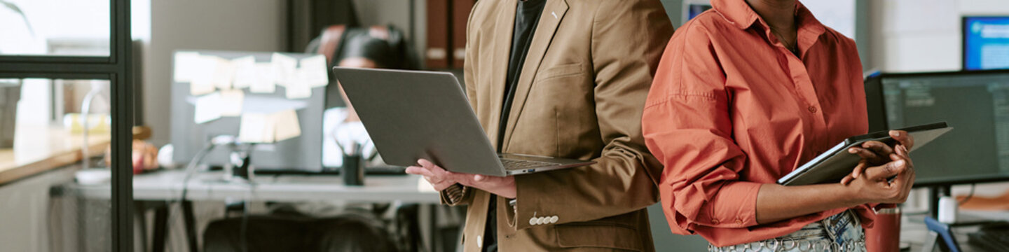 Website banner of woman and man holding tablet and laptop, collaborating in office on digital workflow and team communication. Ideal for business technology marketing, wide shot