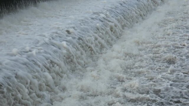 A powerful, high-impact shot of a heavy water torrent crashing down a dam spillway, showcasing the intense kinetic energy and thunderous white foam of nature.
