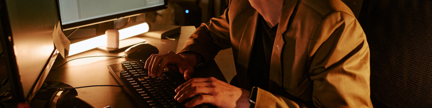 Website banner of programmer typing on desktop keyboard at workstation, managing late night digital tasks and office workflow. Ideal for remote work, productivity, corporate technology use