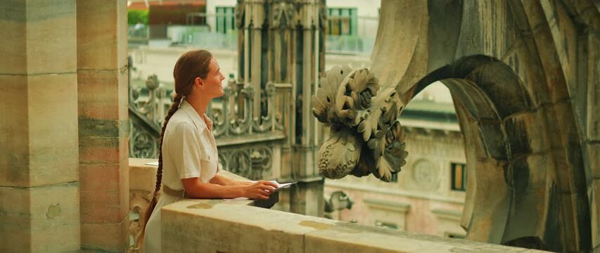 Female traveler studies city view from rooftop terrace of Milan Cathedral holding map