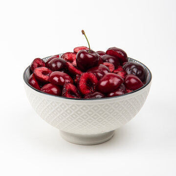 Cerises fra&icirc;ches coup&eacute;es en morceaux dans un bol en c&eacute;ramique blanc, vue en plong&eacute;e - fond blanc