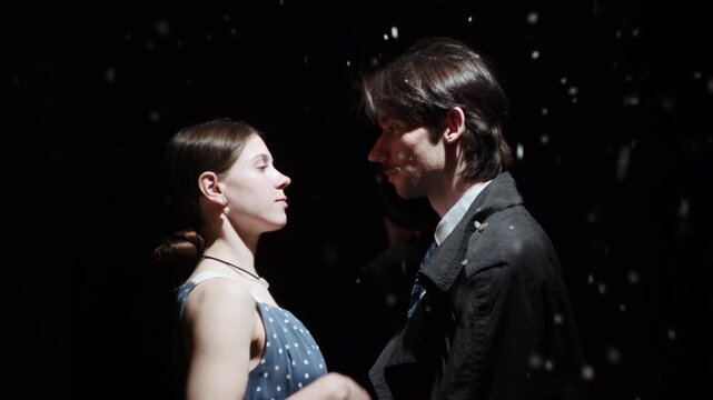 Dramatic theatrical encounter between a man and woman under spotlight with drifting particles