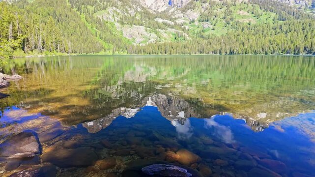 Calm waters of Bradley Lake perfectly mirror the rugged snowcapped Teton peaks above