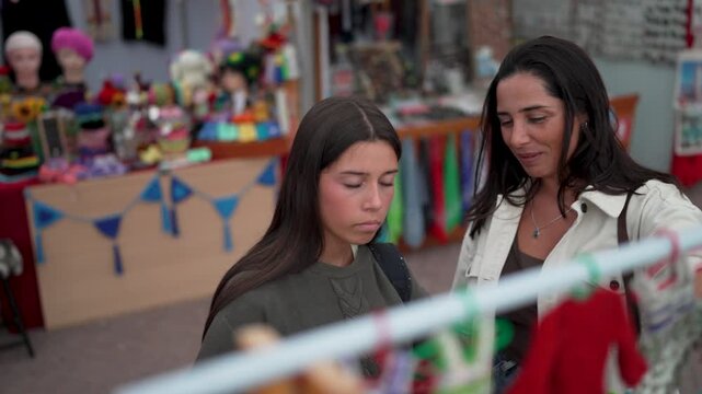 Happy mother and daughter choosing clothes together at a local market stall, enjoying their time