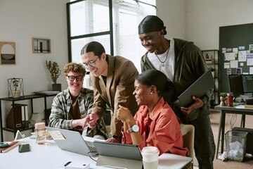 Plakat Diverse young adult team collaborating around laptop, reviewing project ideas and sharing feedback in office. Ideal for workplace teamwork, startup culture, innovation marketing