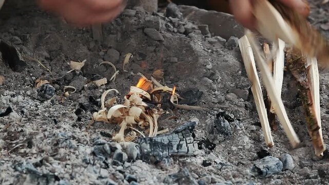 Close up of a person's hands lighting a primitive campfire using kindling and wood. Historical reenactment of 7th-11th century survival skills.