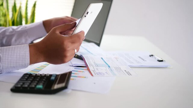 Bill payment concept. Online internet banking. A young Asian man holding a paper receipt or invoice, using a smartphone with a calculator app to calculate monthly expenses. Financial technology.
