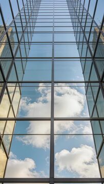 Vertical video: Drifting clouds shifting across glass atrium, mullions showing towers from wind