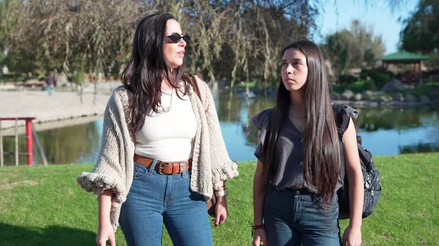 mother and her teenage daughter talking and pointing out while walking in a beautiful park on a sunny day