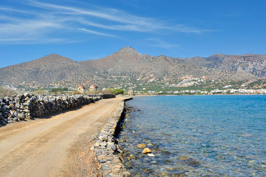 A dirt road in Kalydon (Spinalonga) peninsula near the Elounda town in Crete, Greece. Beautiful blue sky with white clouds in the background.