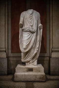 A headless marble statue with detailed toga folds in a museum setting.