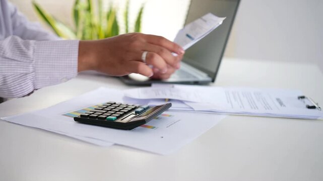 A male accountant holds an invoice and calculates with a calculator. He analyzes expenses, bills, and finances at his desk.
