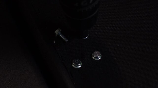 A man's hands unscrewing shiny steel bolts from furniture using electric drill with a socket adapter