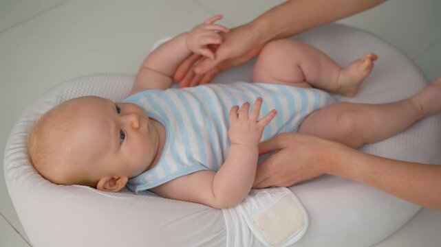 Mother unfastening baby from soft baby nest on floor.