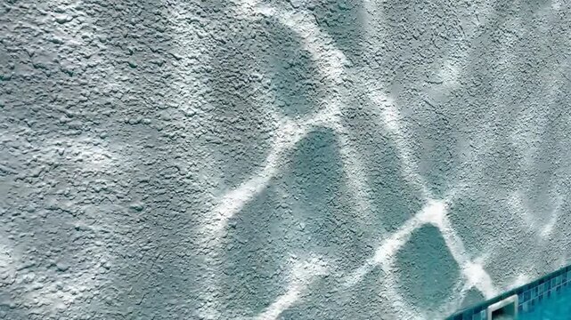 Sunlight patterns on a textured pool wall with turquoise water and a tiled edge dancing stock