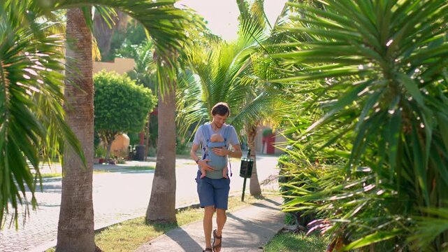 Father and baby son walking beside lush tropical greenery. Slow motion.