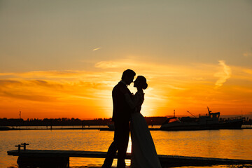 Fototapeta premium Wedding couple silhouette embracing at sunset on marina pier