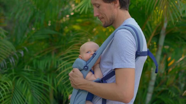 Father walking with baby son in ergonomic baby carrier. Close-up. Slow motion.