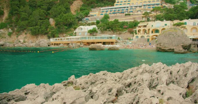Coastal village buildings on cliffs by turquoise sea at Marina Piccola beach in Capri