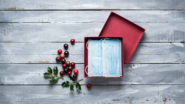 Medical face masks inside a red gift box with autumn berries on a rustic wooden board background