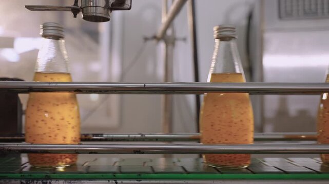 Juice in glass bottles on an automated conveyor belt in a modern beverage production facility line. Technology in the food and drink industry. Ready to drink fruit juice in a manufacturing factory. 