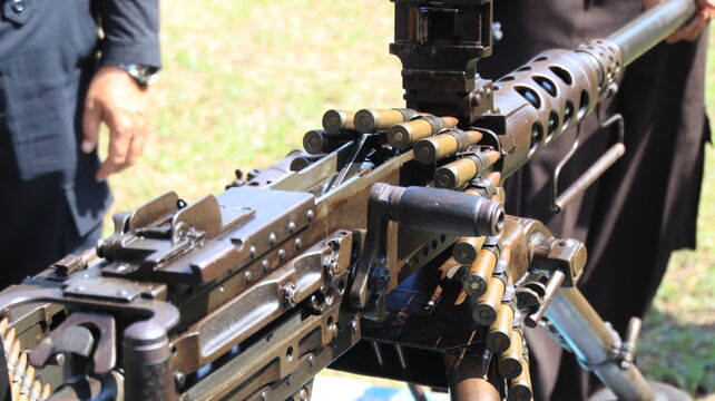 A close up of a belt fed machine gun loaded with ammunition during a military equipment display, highlighting firearm mechanics, defense technology, and operational readiness.