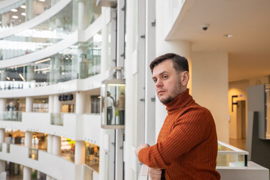 Man standing in modern glass office building. Thoughtful businessman looking at atrium. Professional worker in turtleneck sweater inside contemporary business center hall lobby space.