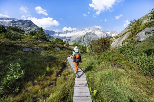 Mountaineers on wooden plank trail through mountain moor, in front of picturesque mountain scenery, Dammastock and Damma glaciers, G&ouml;scheneralp, Canton of Uri, Switzerland