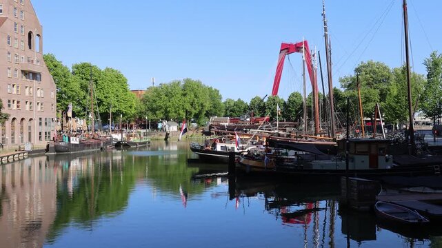 View of the Willemsbrug bridge and traditional boats moored in the Oude Haven harbor with historic brick buildings and green trees in Rotterdam, Zuid-Holland, Netherlands.