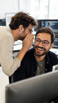 Colleagues laughing and sharing secrets in modern office environment