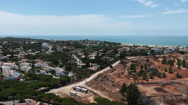 Aerial overview of Quinta do Lago resort buildings in Vale de Lobo, Algarve, Portugal, Europe. Shot of rooftops of luxury cottages in green landscape with mountains on background. Golf fields.