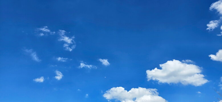 A bright azure sky with scattered fluffy white clouds. Cumulus clouds are on the right side of the image. Clear and sunny weather. Cirrus clouds appear as thin streaks on the left side of the image 
