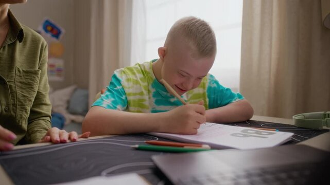 Caucasian boy with Down syndrome writing in notebook while his mother supporting hem and helping. Ideal for promoting inclusive education, special needs support, and social diversity