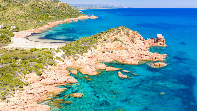 Aerial drone view of the Marina di Gairo coastline, Sardinia. Turquoise Mediterranean waters meet striking red granite cliffs, creating a wild and unspoiled coastal landscape.