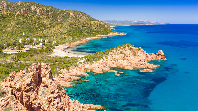Aerial drone view of the Marina di Gairo coastline, Sardinia. Turquoise Mediterranean waters meet striking red granite cliffs, creating a wild and unspoiled coastal landscape.