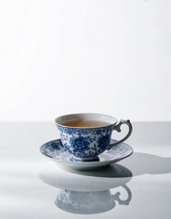 Fototapeta premium Vintage blue and white floral porcelain teacup with matching saucer on a reflective surface