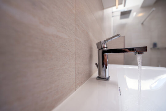 modern bathroom with shower. Open Water Faucet with flowing water at luxury bathroom. Minimalist water faucet against a blue backdrop, showcasing the flow of tap water in a clean, modern design.