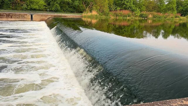 Rushing water flowing over a concrete river weir against green trees