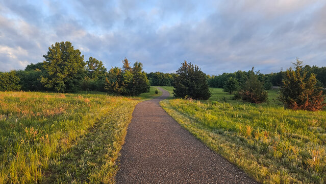 a paved asphalt path winding through a rural landscape with open fields and trees. renewal afer a controlled burn.