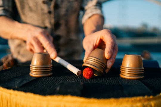Man Performs Cup and Ball Trick in Outdoor Setting During Evening