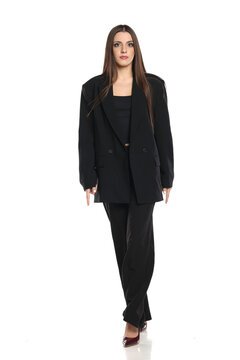 Studio shot of serious brunette business woman in black blazer and pants, full body, on white background.