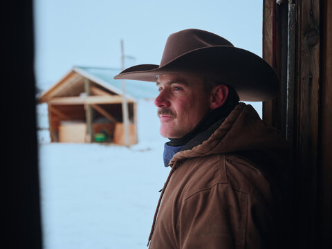Cowboy Stands at Door of Cabin in the Snow During Winter Time