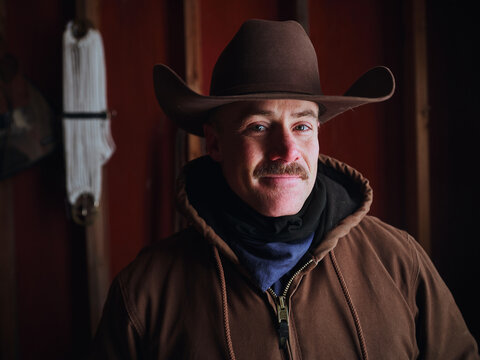 Cowboy Stands Inside Barn Wearing Hat and Warm Clothes During Winter