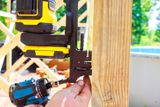 Frame worker clamps laser level to wooden post drills it at construction site