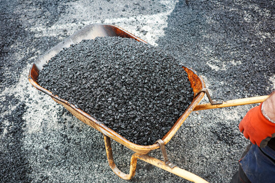 Worker pushing wheelbarrow full of fresh asphalt