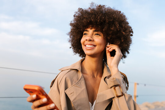 Smiling woman with afro hair using wireless earbud