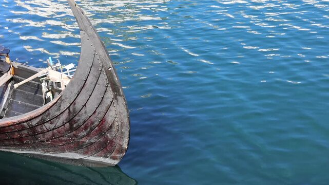 View of the wooden bow of a traditional Viking ship replica floating on the calm blue water of the harbor in Alesund, More og Romsdal, Norway.