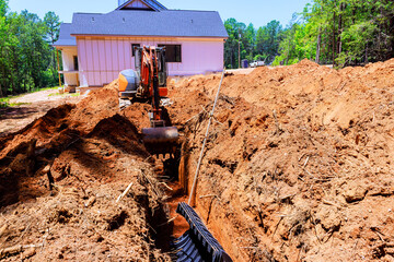 Heavy excavator works to create trench next to house during install drainage septic chamber pipe © ungvar
