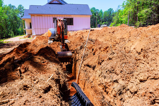 Heavy excavator works to create trench next to house during install drainage septic chamber pipe