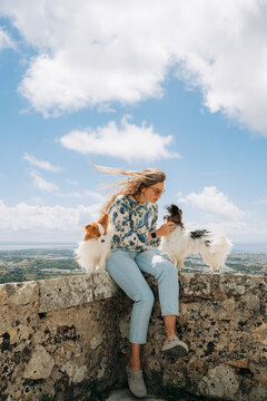 Woman with two fluffy dogs relaxing on stone wall under cloudy s
